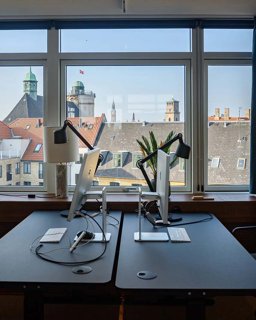 To arbejdspladser ved et vindue med udsigt over Københavns tage og tårne